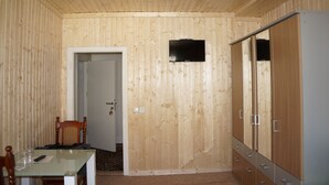 A room with wooden panel walls, a television mounted on the wall, a wardrobe, and a door leading to another room. - Pension Aksaray (Feldkirch)
