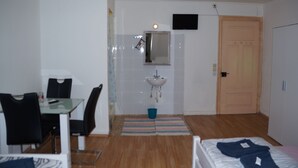 A room with a bed, a desk with a chair, a sink, a mirror, and a television on the wall. - Pension Aksaray (Feldkirch)