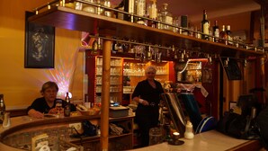 A bar area with shelves of bottles and glasses, a bartender, and a customer. - Pension Aksaray (Feldkirch)