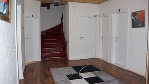 A hallway with a wooden floor, a checkered rug, white doors, and a staircase with red steps. - Pension Aksaray (Feldkirch)