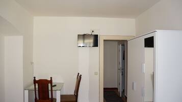 Ein Zimmer mit Esstisch, zwei Stühlen, einem flachbildfernseher an der Wand und einem weißen Kleiderschrank.