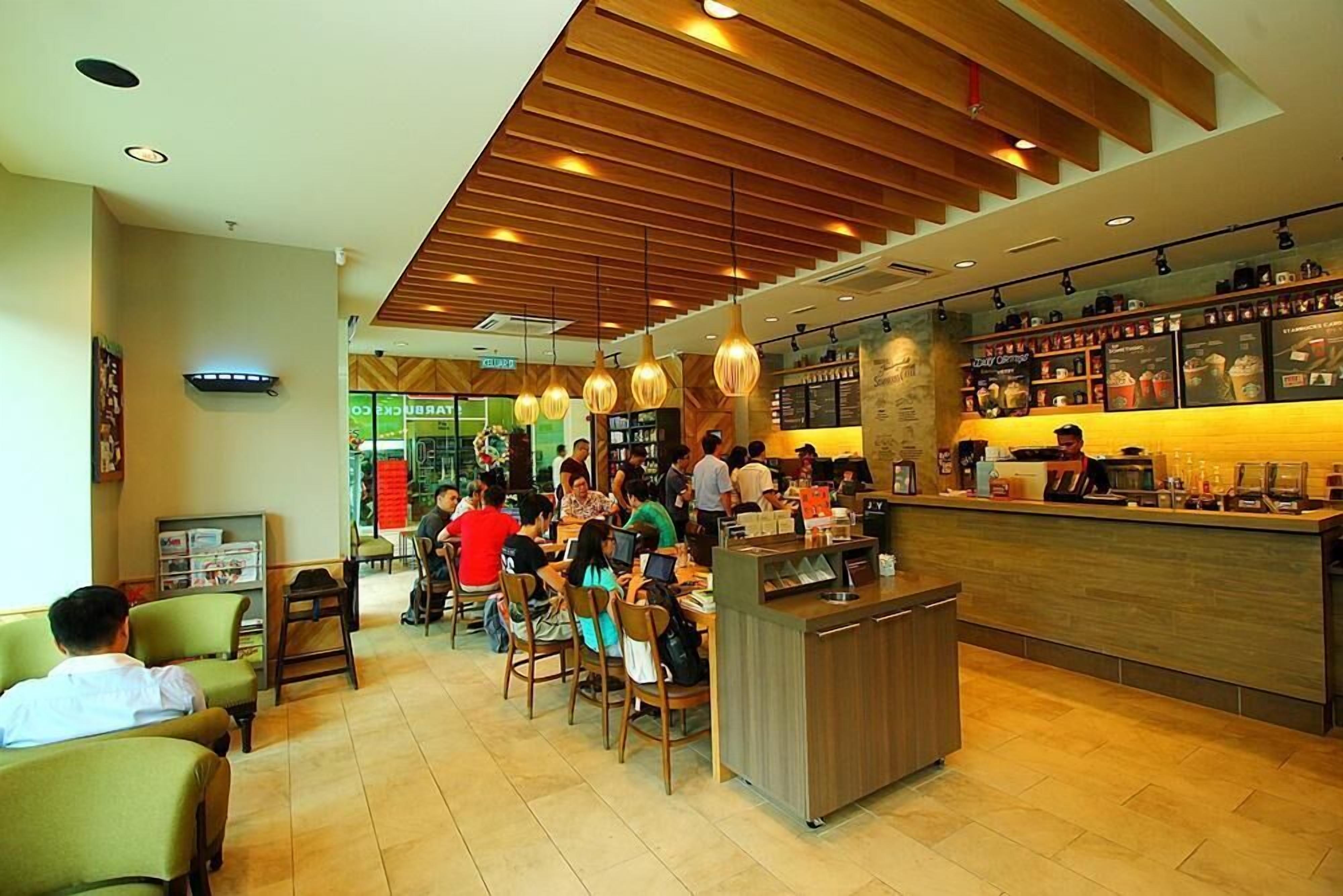 A modern cafe with wooden ceiling panels, a counter with a menu, and several patrons seated at tables.