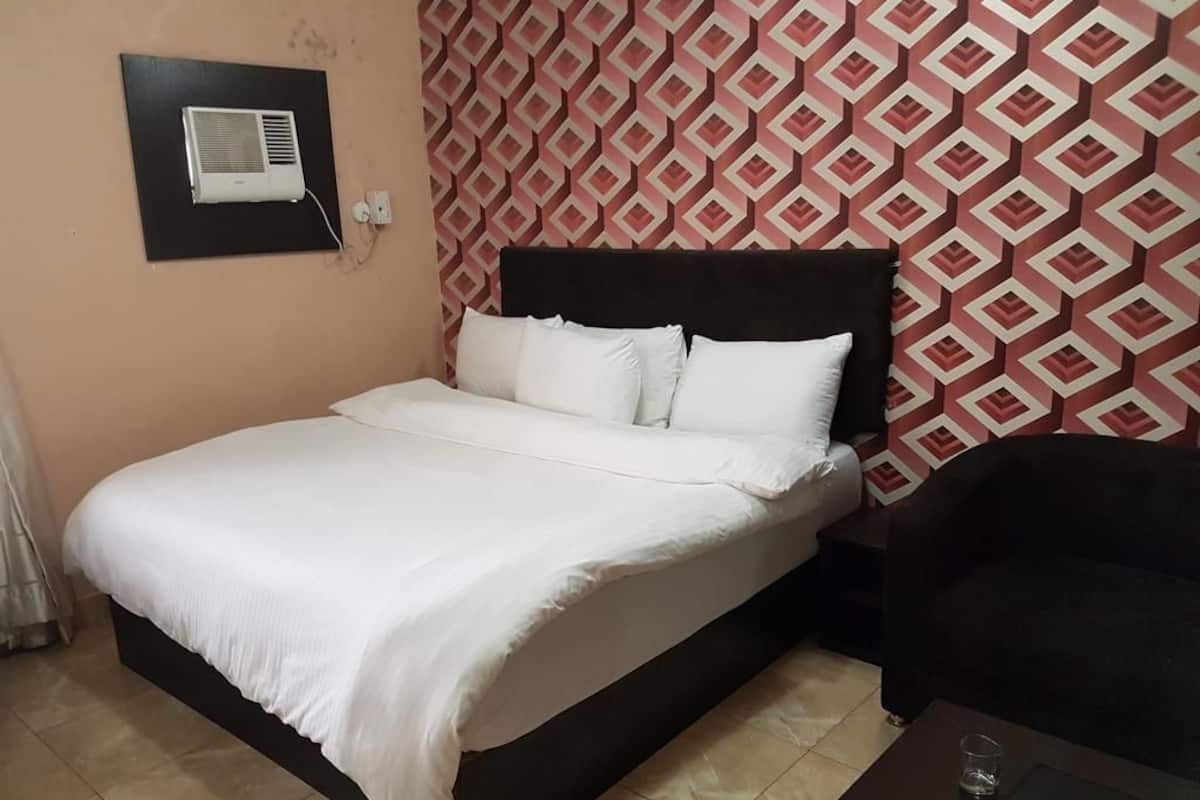 Una cama bien hecha con sábanas blancas, cabecera oscura y pared estampada al fondo.
