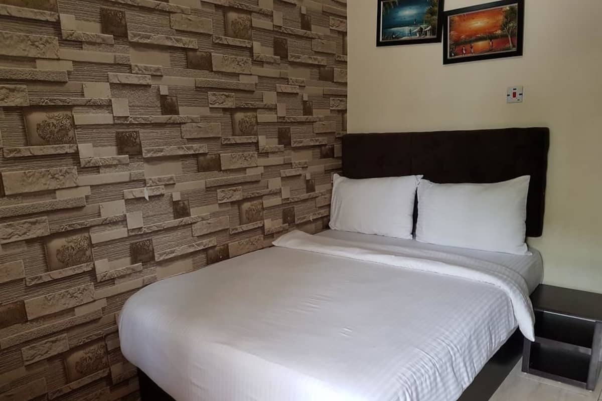 Una cama cuidadosamente arreglada con un cabecero oscuro en una habitación con pared de diseño de piedra y dos cuadros colgados encima.