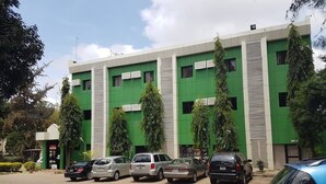 A multi-story building with a green facade, parked cars in front, and a clear sky. - Eddy Vic Hotel (Abuja)