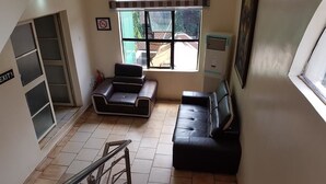 A spacious living area with a staircase, two black leather sofas, a large window with a view of the outside, and a fire extinguisher on the floor. - Eddy Vic Hotel (Abuja)
