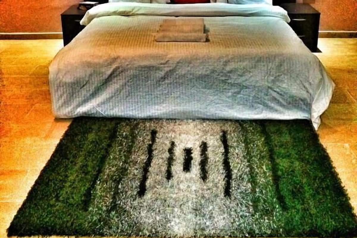 Un dormitorio con una cama grande, dos mesitas de noche, un almohadón rojo y dos cuadros enmarcados en la pared.