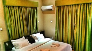 A hotel room with a bed, a nightstand, an air conditioning unit, and green curtains. - The 09 Suites (Abuja)