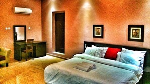 A hotel room with a bed, a desk, and a chair. There is an air conditioning unit on the wall. - The 09 Suites (Abuja)