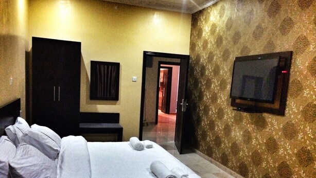 A hotel room with a bed, a TV mounted on the wall, and a wardrobe. - The 09 Suites (Abuja)