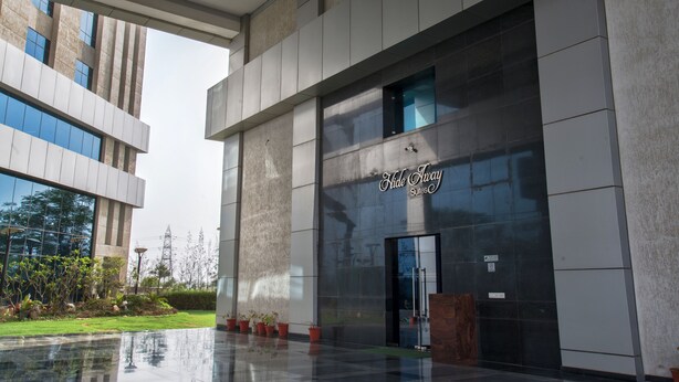 A modern building with a glass facade and a sign for "Hide Away Suites." - Hide Away Suites (Noida)