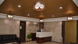 A reception area with a reception desk, a receptionist, a dark leather sofa, and a coffee table. - Hide Away Suites (Noida)