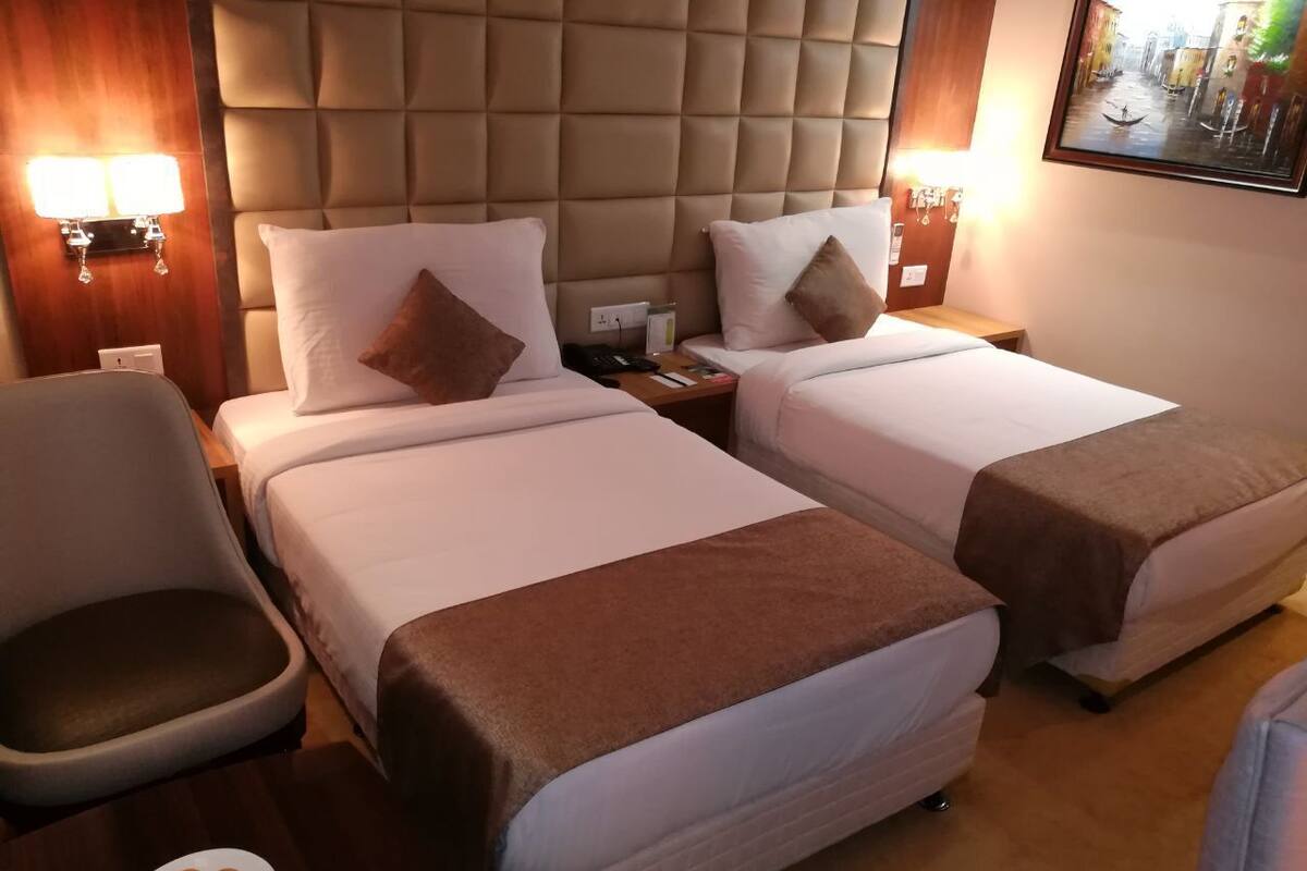 A hotel room with two beds, a chair, a nightstand, and a wall-mounted lamp.