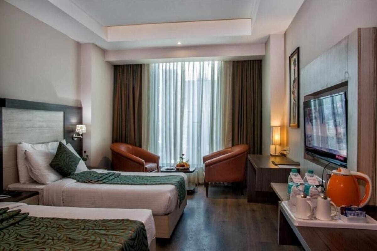 A hotel room with two beds, a TV, a desk with a chair, a coffee maker, and a window with curtains.