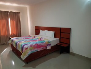 A neatly made bed with a colorful bedspread, a wooden headboard, and a bedside table with a lamp. - De George's Grand Resort (Karu)