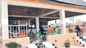 Un espace de café en plein air avec des tables et des chaises, un sol carrelé et un coin salon abrité.