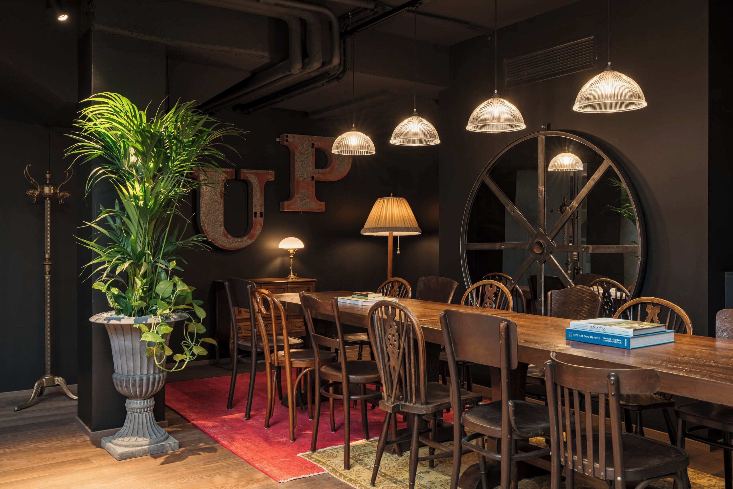Un comedor con una mesa de madera, sillas, una planta en maceta y lámparas colgantes.