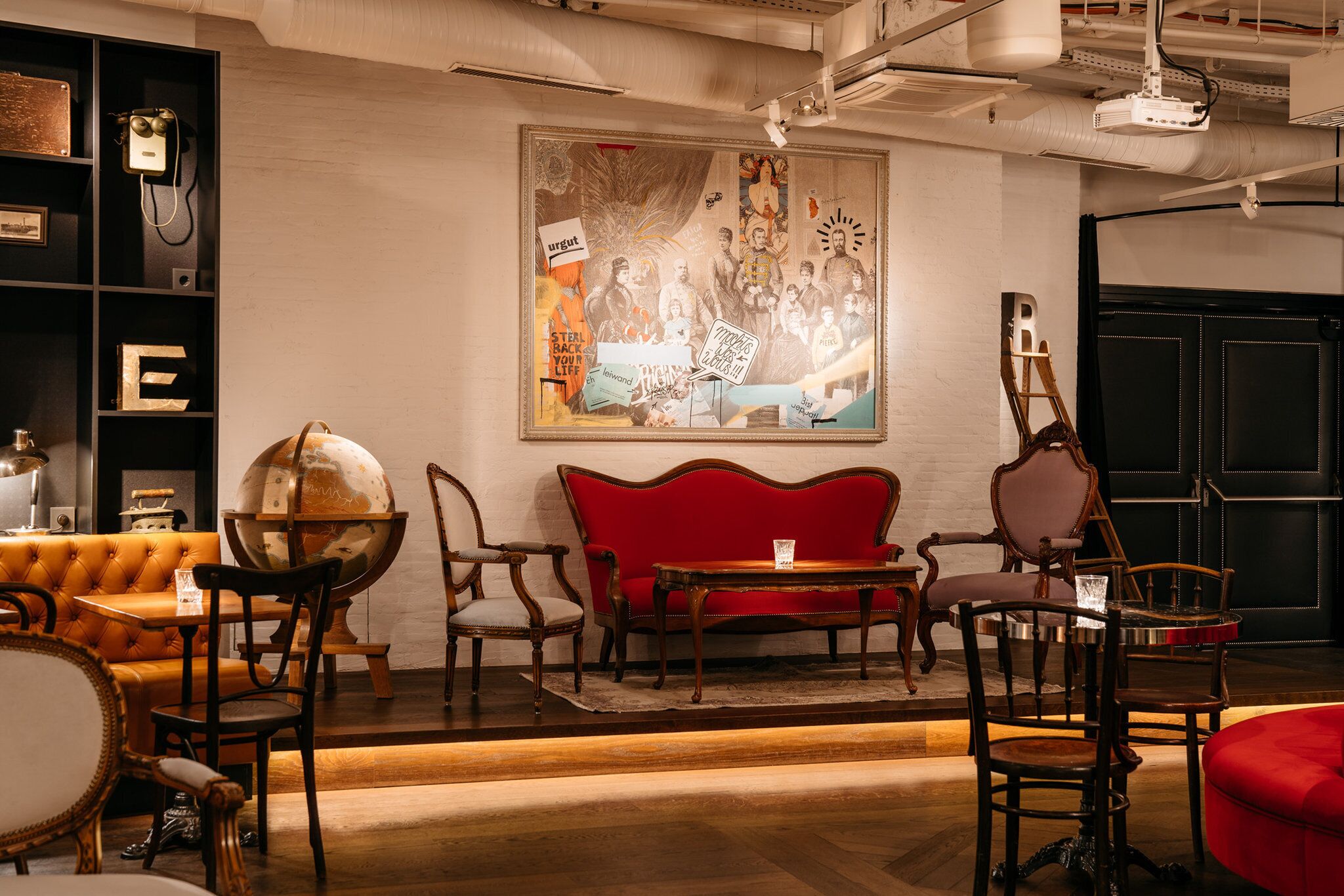 A room with a red sofa, wooden chairs, a globe, and a framed artwork on the wall.