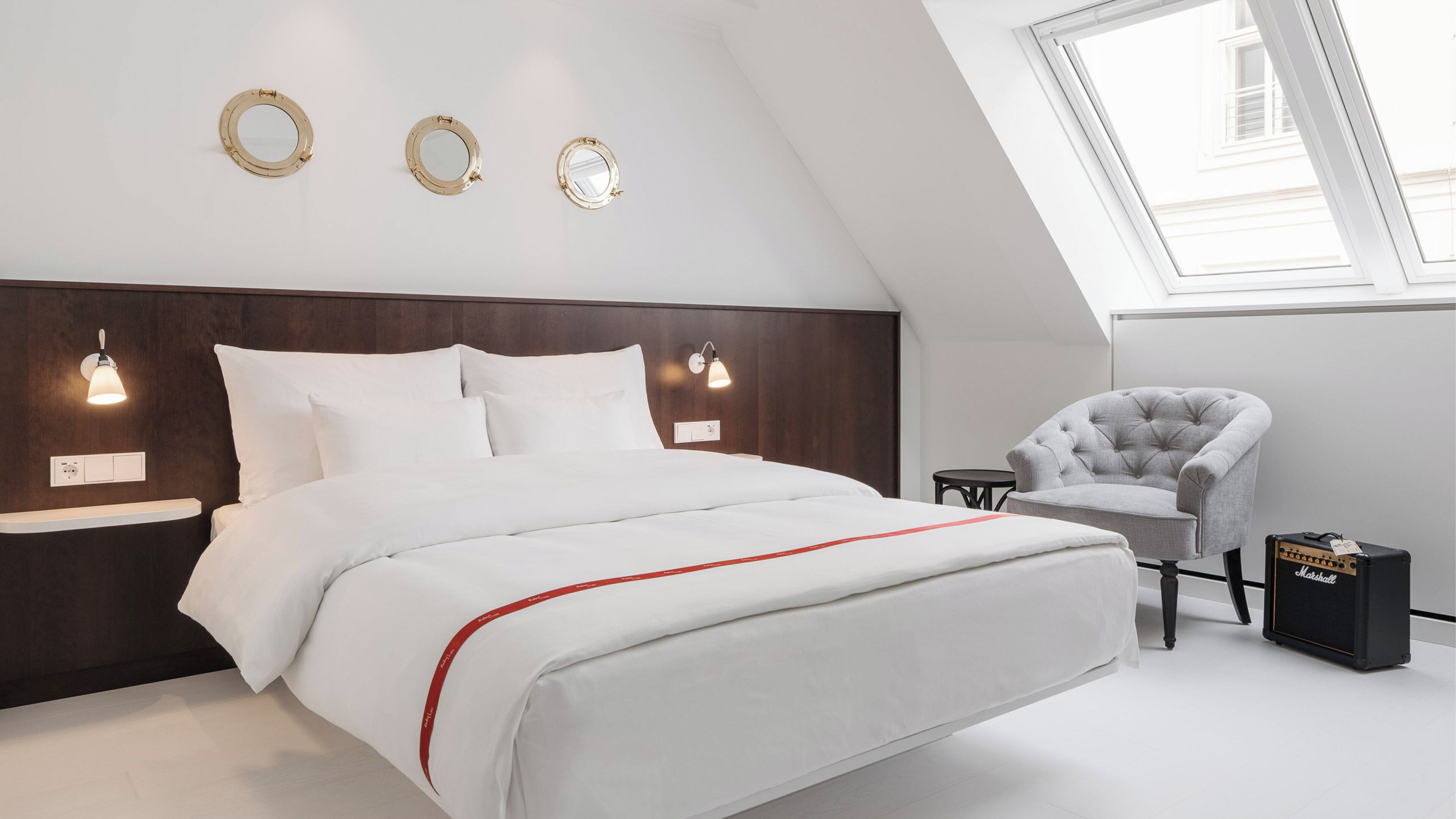 A modern bedroom with a large bed, a vanity with a mirror, a chair, and a Marshall amplifier.