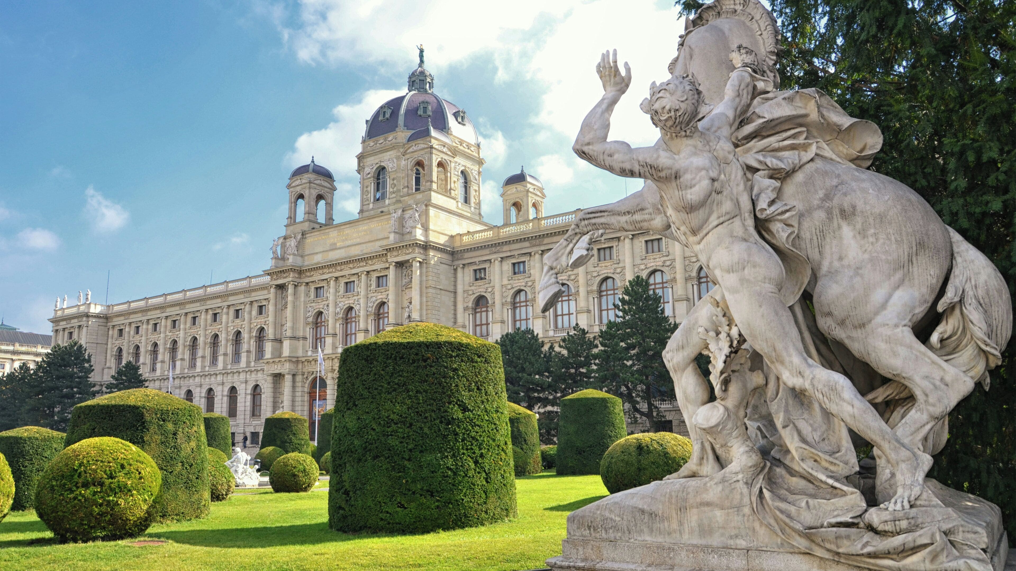 A large building with a prominent dome and statues in the foreground.