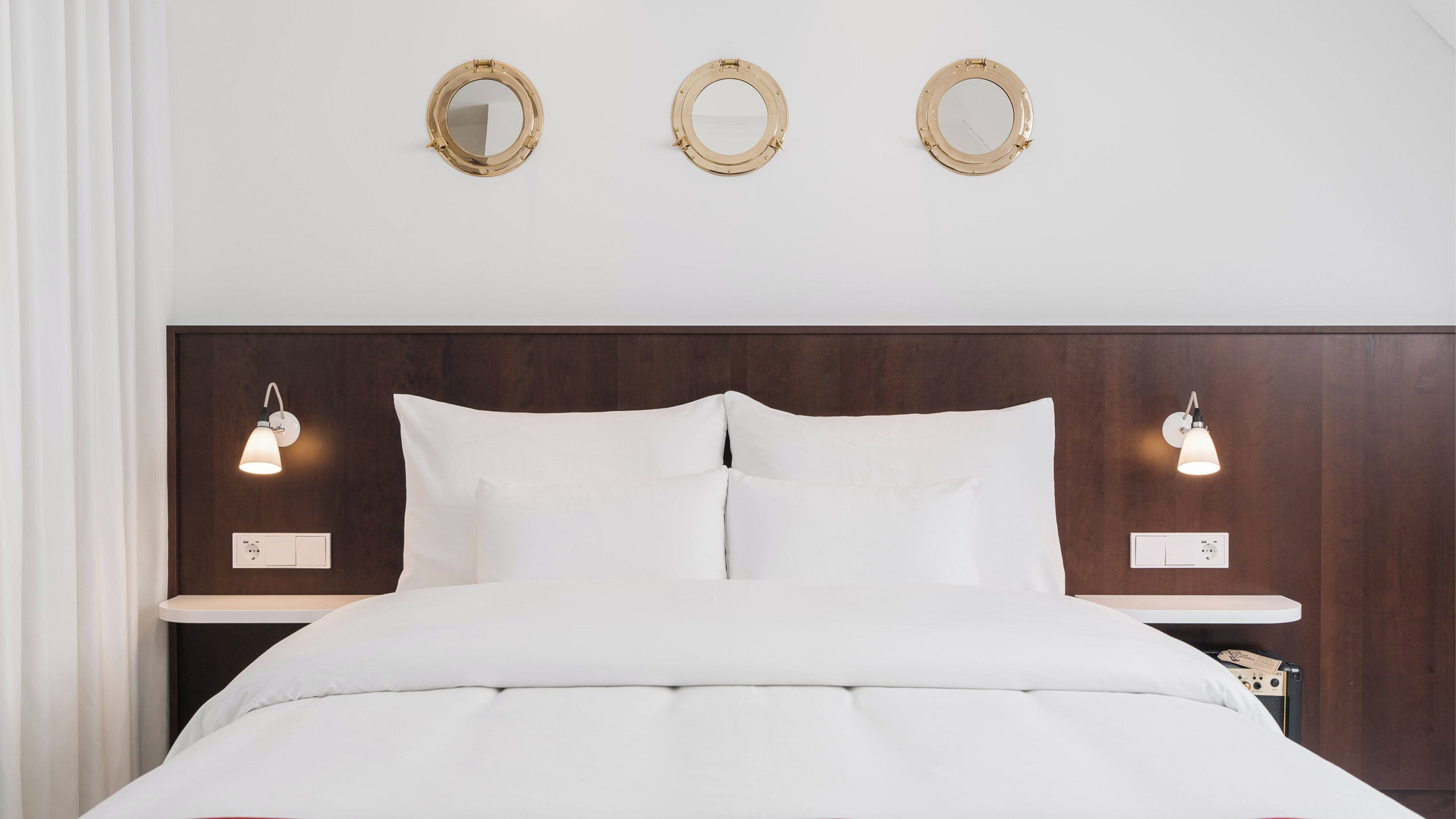 A neatly made bed with white bedding, a wooden headboard, and three round mirrors on the wall above.