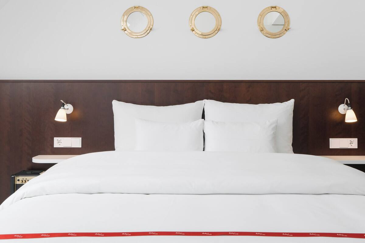 A neatly made bed with white bedding, two bedside tables with lamps, and three wall-mounted mirrors.