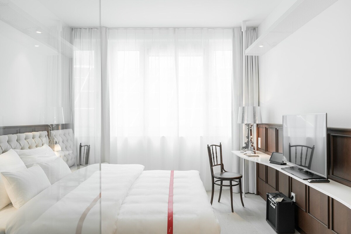 A modern hotel room with a large bed, a desk with a laptop, a chair, and a TV.
