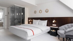A modern hotel room with a large bed, a glass-enclosed shower, a wooden headboard, and a seating area with a chair and table. - Ruby Lissi Hotel Vienna by IHG (Vienna)