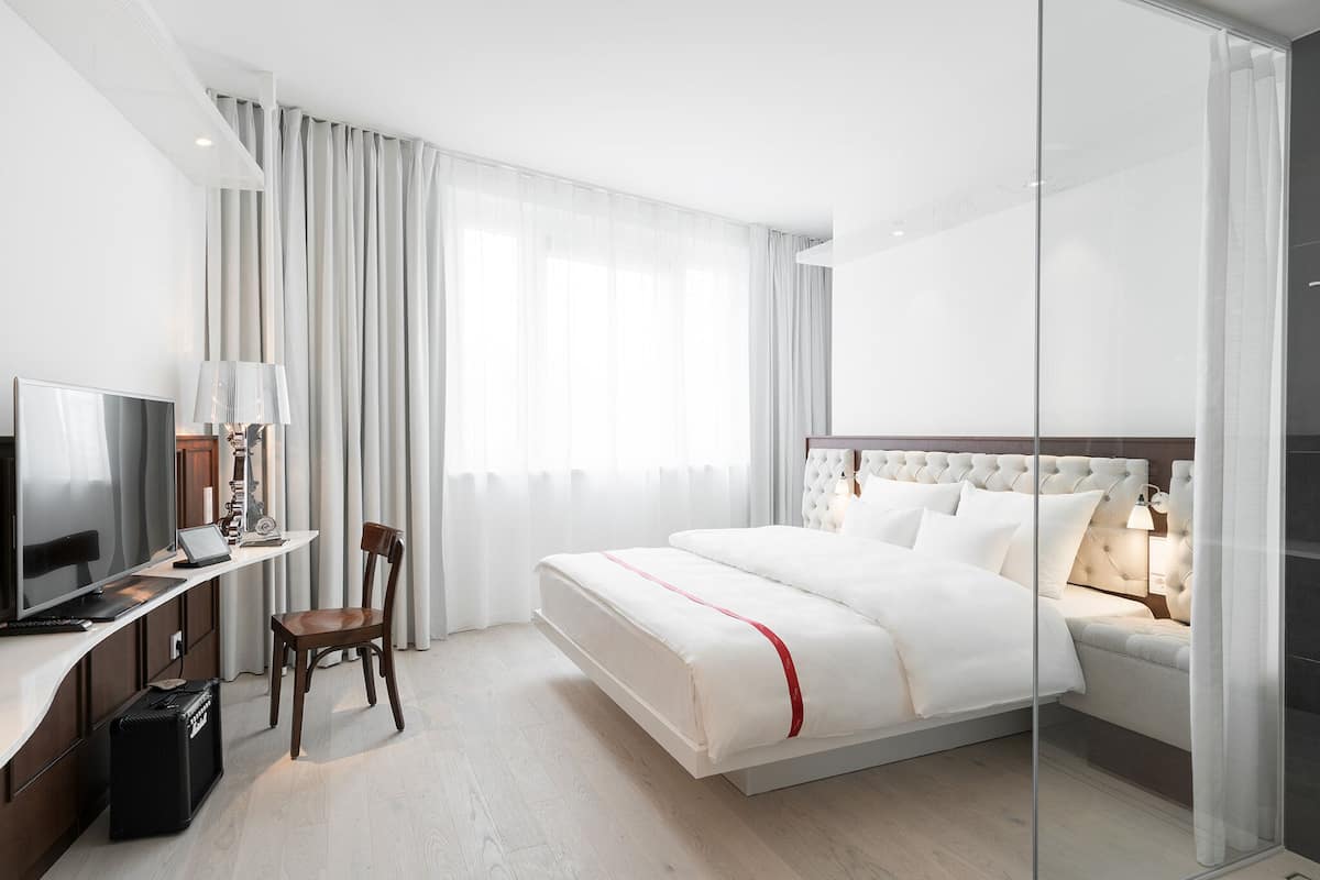 A hotel room with a bed, a desk with a computer, a chair, and a television.