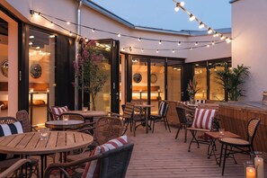 An outdoor patio with wooden tables and chairs, string lights, and potted plants. - Ruby Lissi Hotel Vienna by IHG (Vienna)