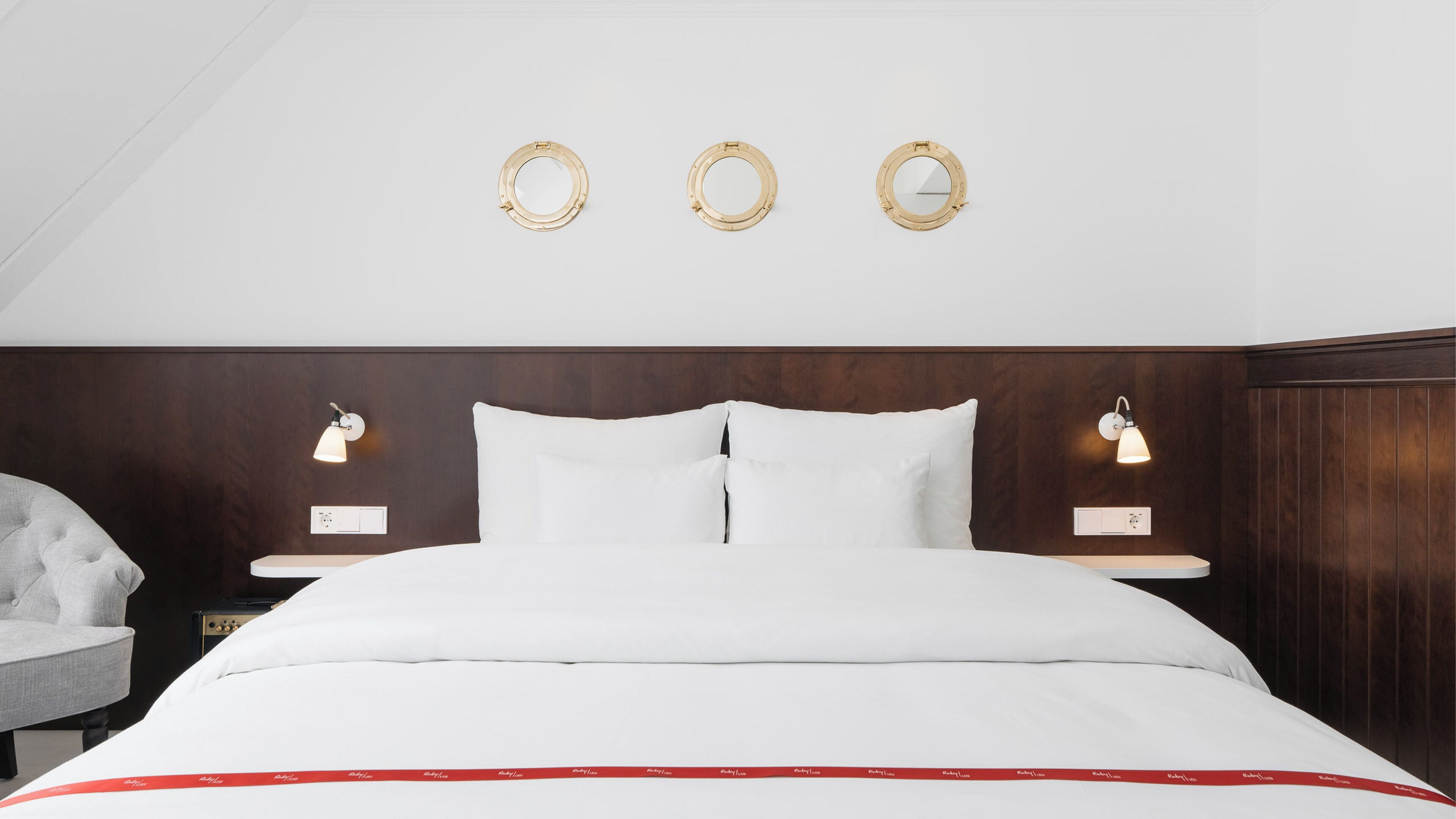 A hotel room with a bed, two bedside tables with lamps, a chair, and a wooden headboard.