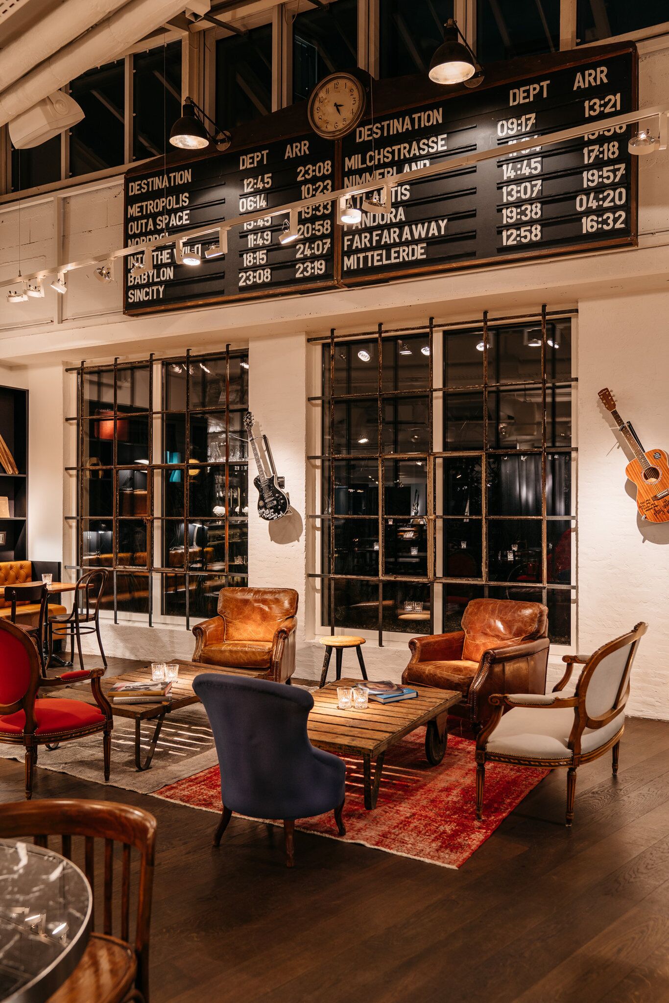 A lounge area with leather chairs, a wooden coffee table, and a large window with a view. A sign above lists destinations and times.