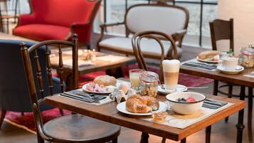 Un desayuno con mesas y sillas de madera, y una variedad de alimentos como cruasanes, huevos y bebidas.