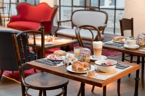A breakfast setting with wooden tables, chairs, and a variety of food items including croissants, eggs, and beverages.