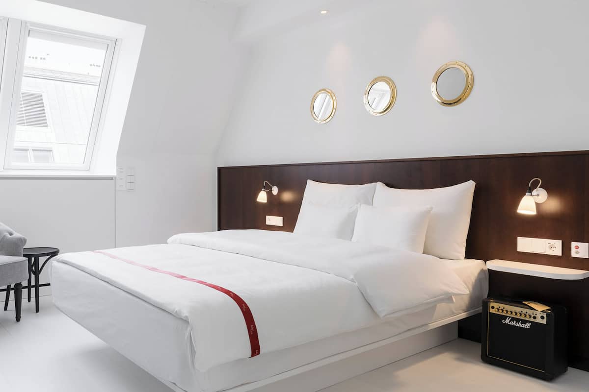 A modern hotel room with a large bed, a grey armchair, a small table, and a Marshall amplifier.