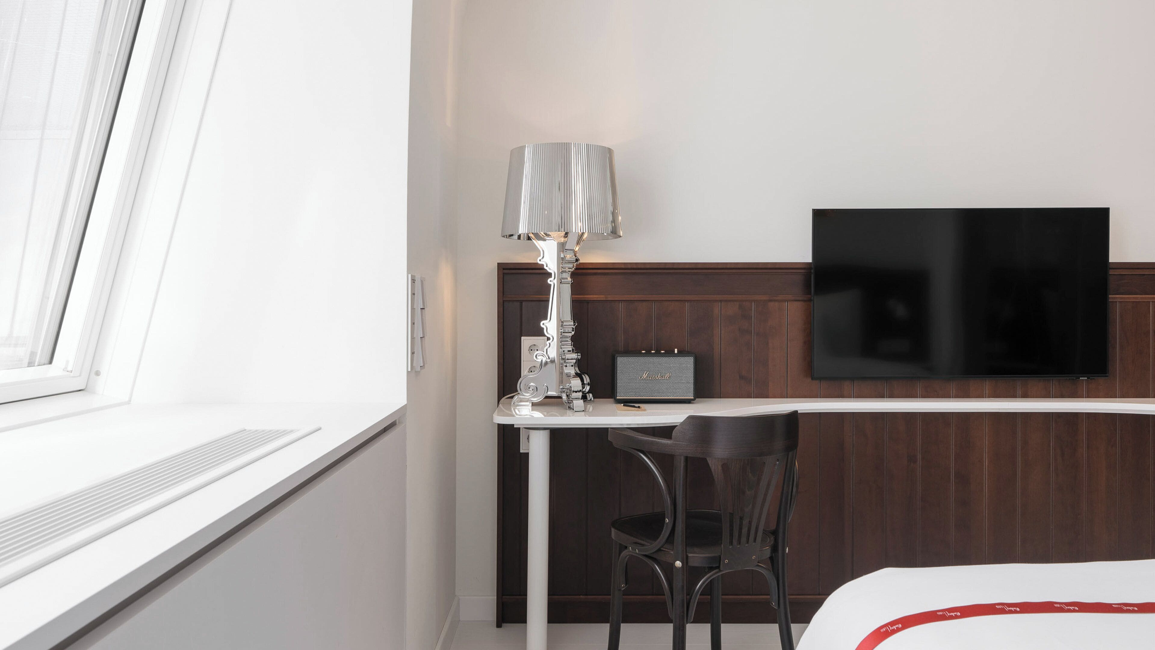 Una habitación de hotel con escritorio, una silla, televisor y ventana.