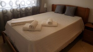 A neatly made bed with rolled towels, a wooden headboard, and a nightstand with a lamp. - Apartamentos Quinta Girassol (Loulé)