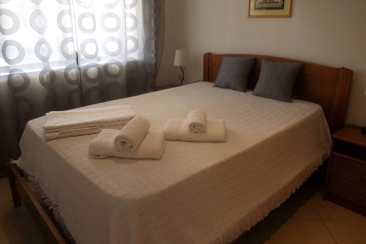 A neatly made bed with rolled towels, a wooden headboard, and a nightstand with a lamp.