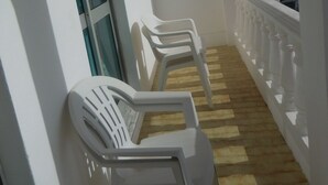 A balcony with white plastic chairs, a window with blinds, and a white balustrade. - Apartamentos Quinta Girassol (Loulé)