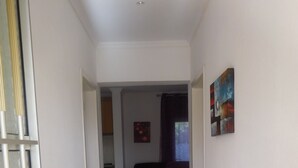 A hallway leading to a living area with a sofa and a painting on the wall. - Apartamentos Quinta Girassol (Loulé)