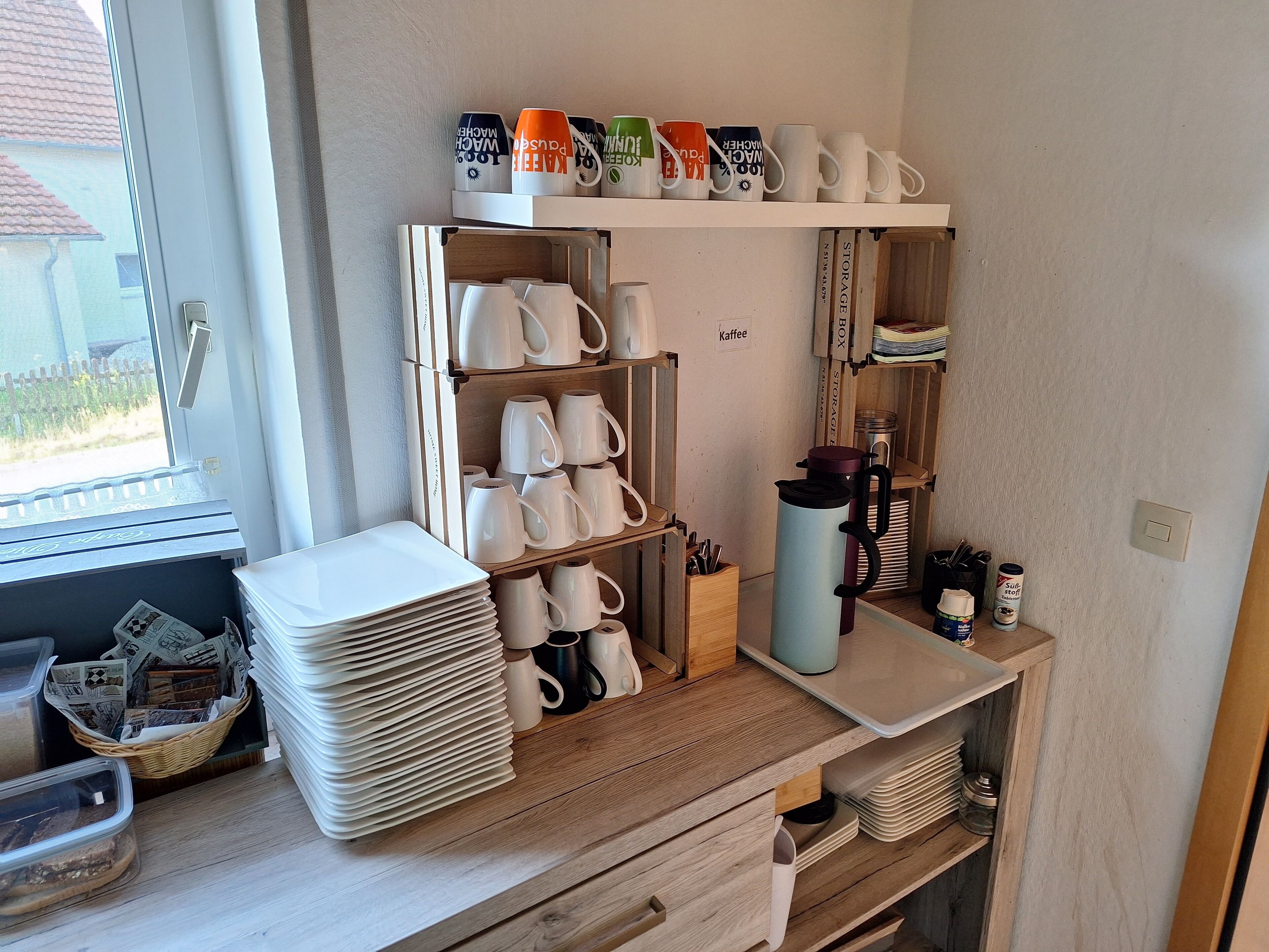 A kitchen with white mugs, plates, and a coffee maker on shelves.