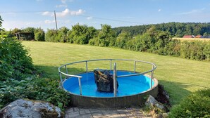 Ein kreisförmiger Pool mit Metallgeländer, umgeben von einem gepflasterten Weg und üppiger Vegetation.