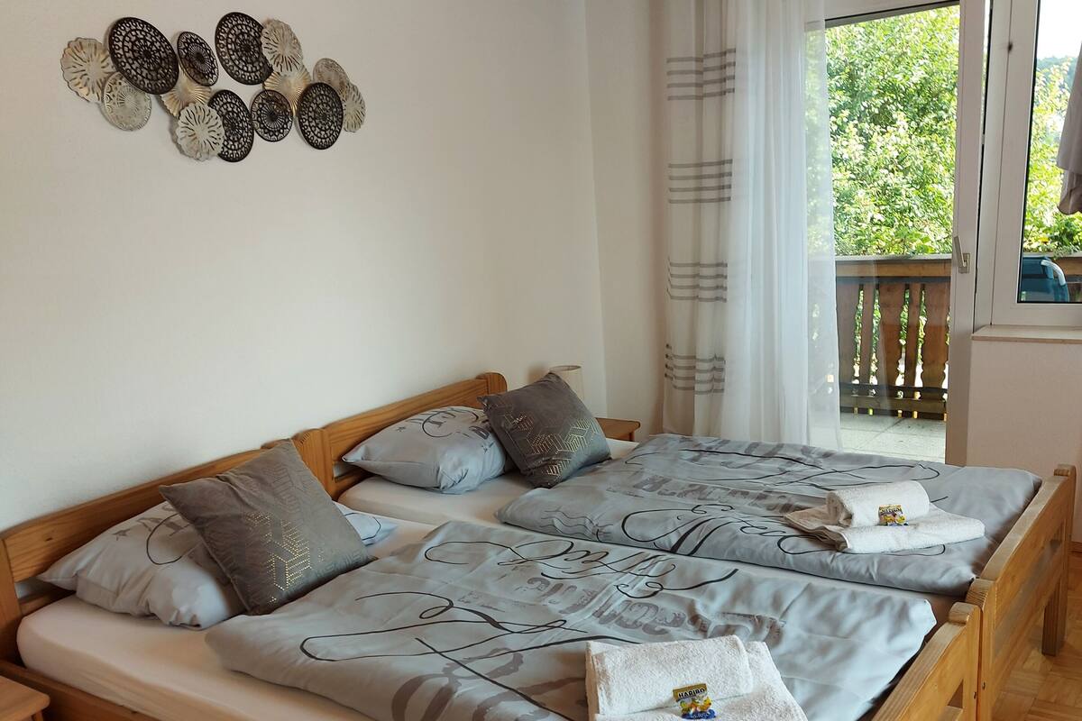 Een tweepersoonsbed met houten frame, twee kussens en een dekbed. Er is een raam met gordijnen, een houten plafond en een wand met decoratieve borden.