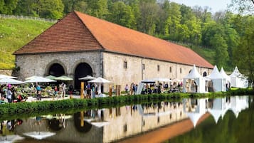 A historic stone building with a red-tiled roof, arched doorways, and a reflection in the water.