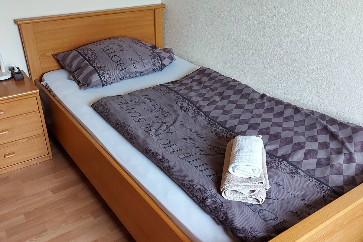 Een eenpersoonsbed met een houten hoofdbord, een geruit dekbed en twee kussens met een patroon.