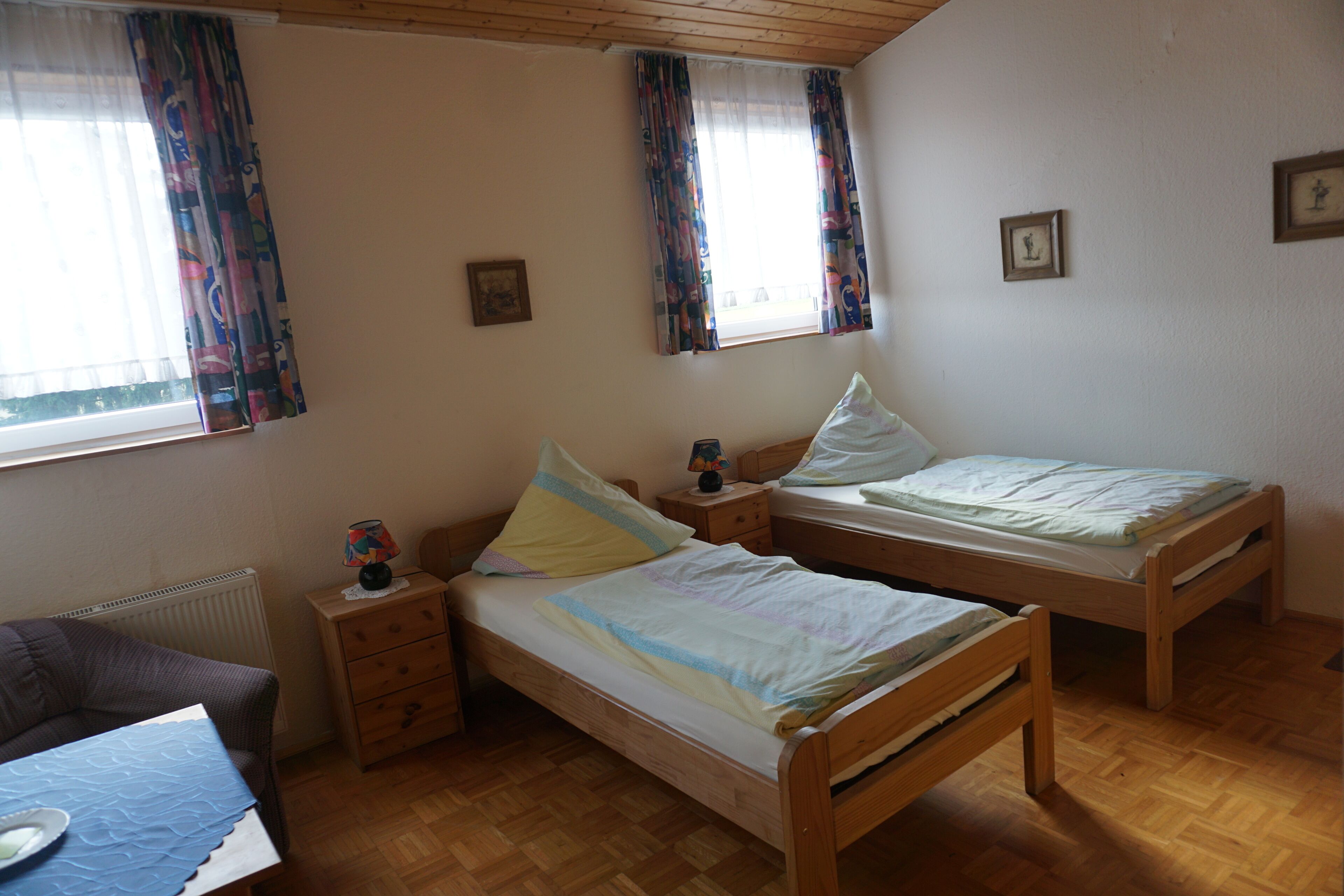 Une chambre avec deux lits en bois, une petite table avec une lampe et une fenêtre avec des rideaux.