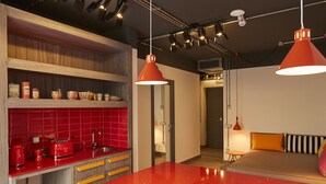A modern kitchen with a red countertop, wooden shelves, and a red island. There are overhead lights and a red pendant light. - Toledo Loft (Naples)