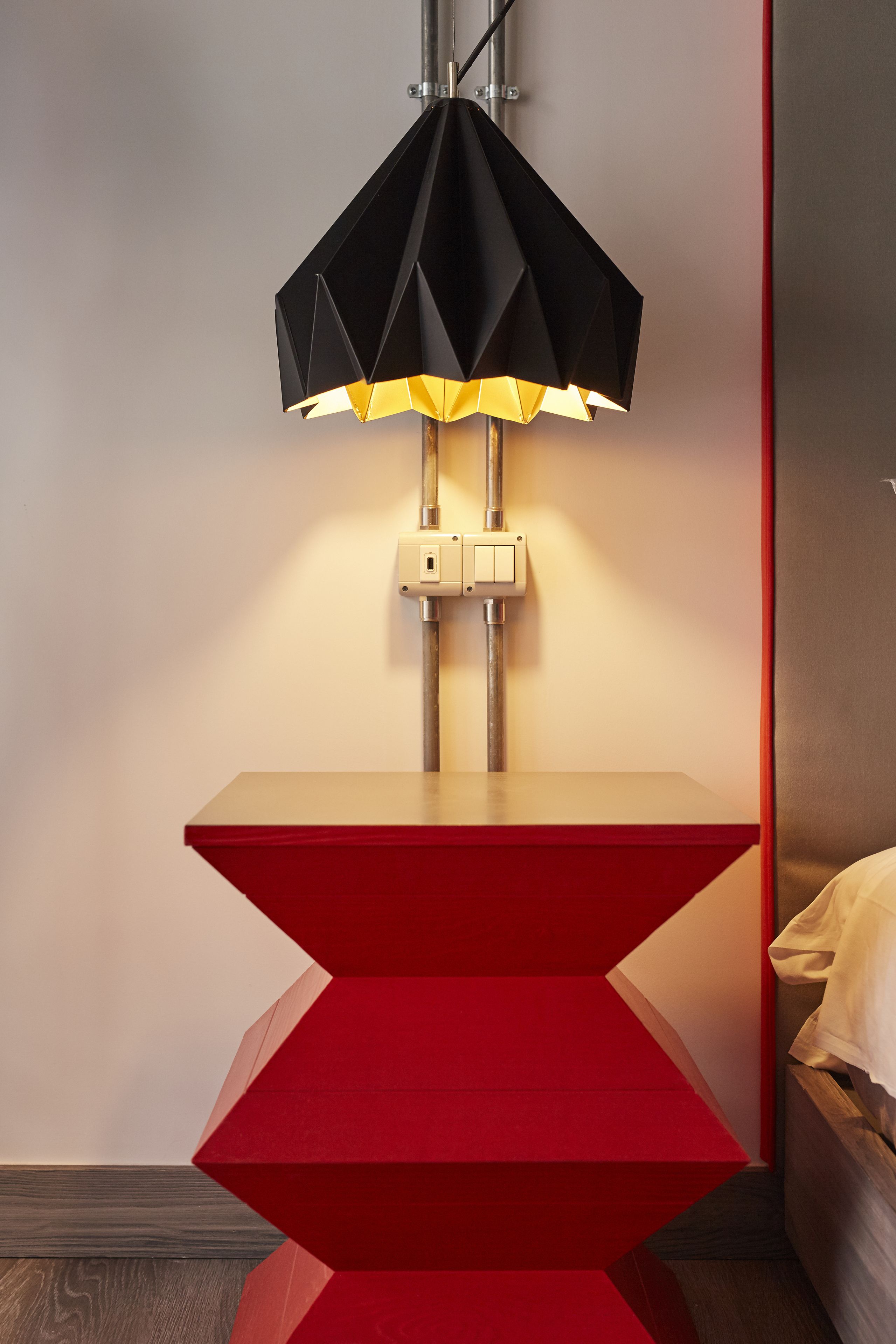 Ett modernt rum med en unik, geometrisk golvlampa, ett sängbord och en säng.