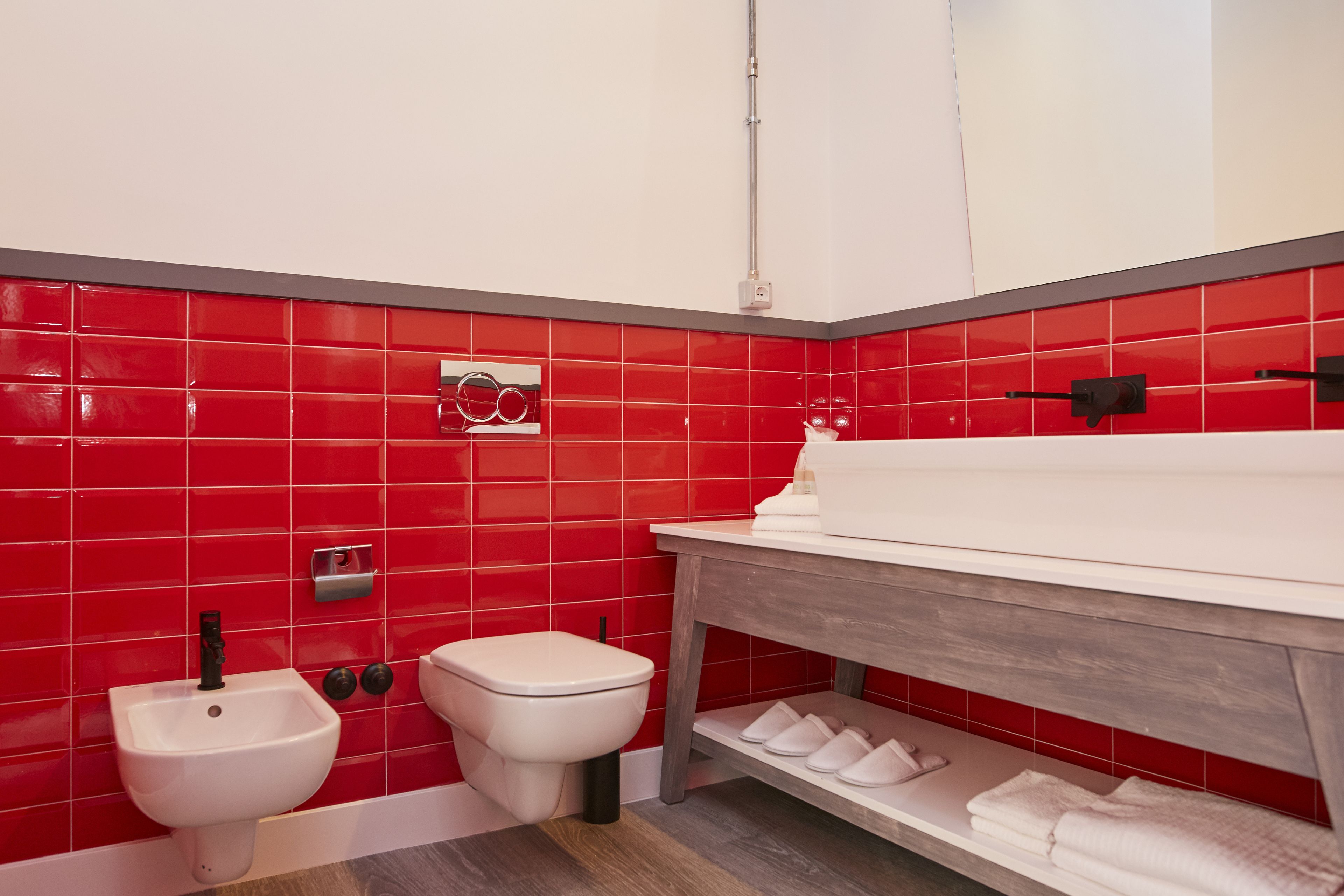 A bathroom with red tiled walls, a white sink, and a bidet.