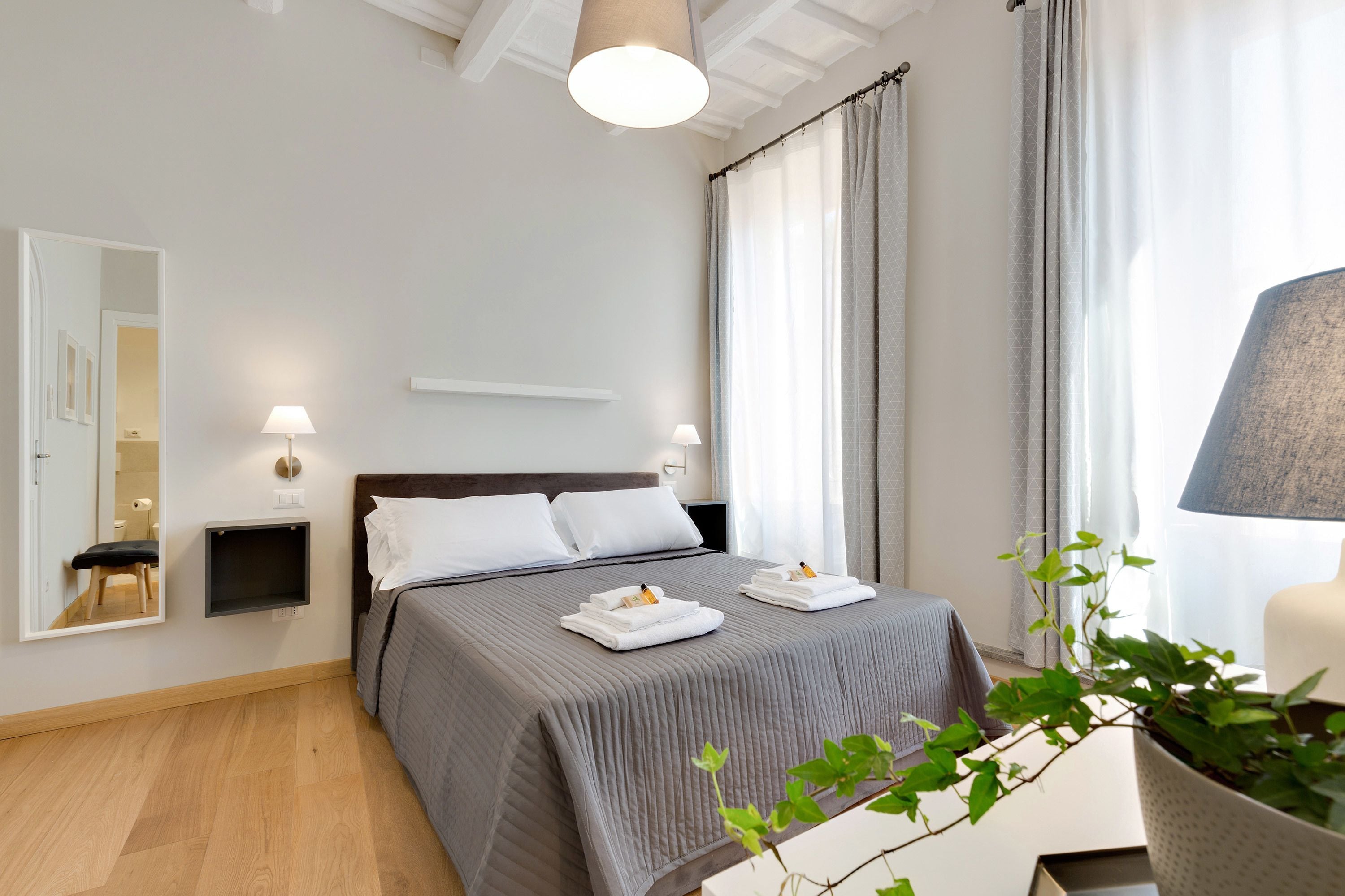 A modern bedroom with a large bed, bedside tables, a mirror, and a potted plant.